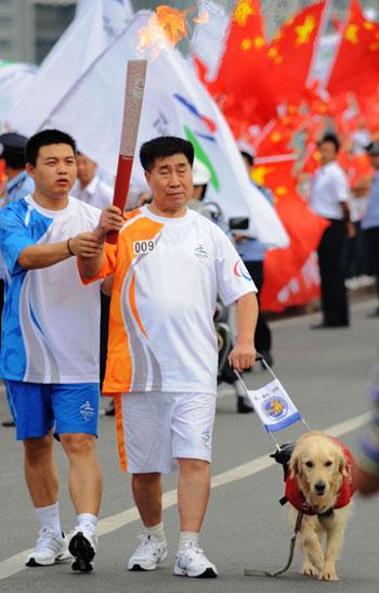 Zhang&nbsp;Dehong&nbsp;(right)&nbsp;holds&nbsp;the&nbsp;Paralympic&nbsp;torch&nbsp;with&nbsp;the&nbsp;help&nbsp;of&nbsp;a&nbsp;torch&nbsp;escort&nbsp;and&nbsp;a&nbsp;guide&nbsp;dog&nbsp;during&nbsp;the&nbsp;Dalian&nbsp;relay&nbsp;on&nbsp;Wednesday.&nbsp;