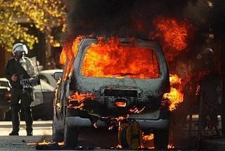 A car burns in front of riot police during a massive demonstration near the main police station in the northern Greek city of Thessaloniki.(AFP/Sakis Mitrolidis)