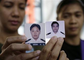 FILE - This Monday April 13, 2009,file photo shows the wives of Filipino sailors, Doris Deseo, left, and Catherine Boretta, right, showing pictures of their husbands Carlo, second from left, and Rodell, second from right, to the Associated Press as they visit the office of a shipping agency in Manila, Philippines on to get updates on negotiations to free their hostage husbands in Somalia. (AP Photo/Aaron Favila)
